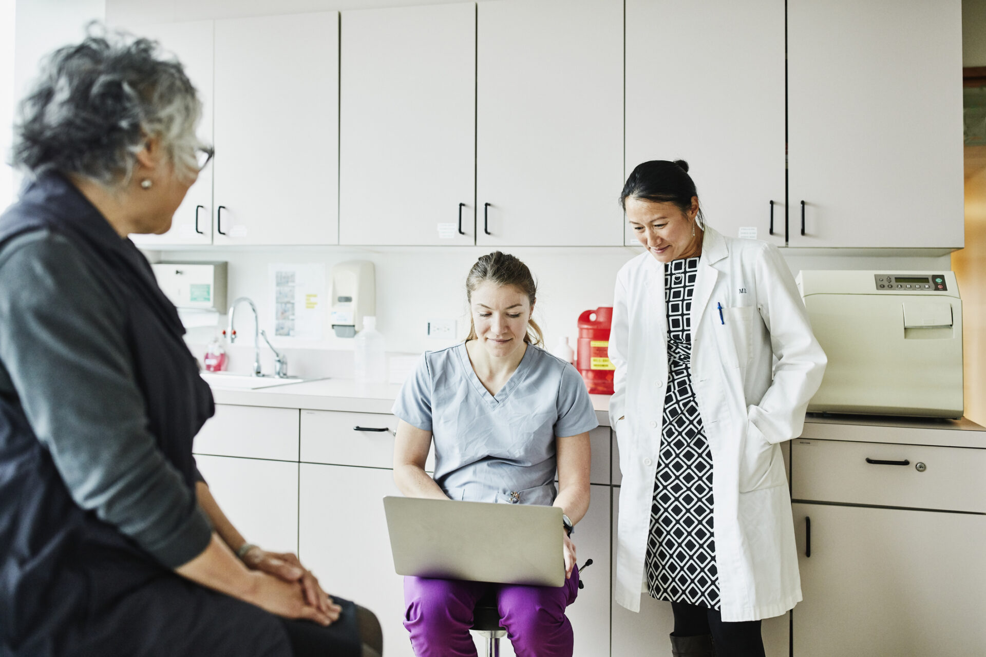 Female doctor and nurse reviewing patients chart on laptop during appointment in exam room