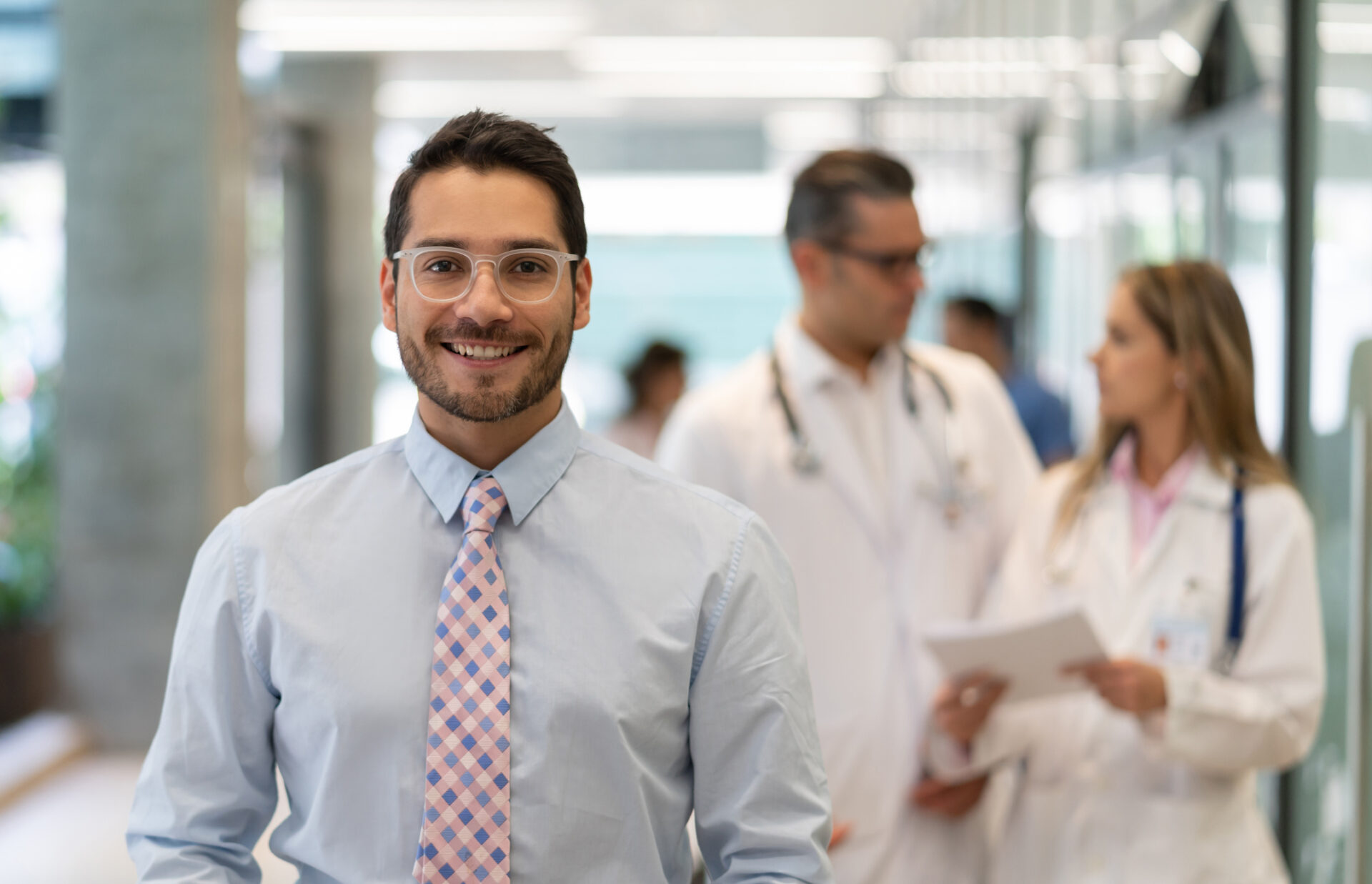 Hospital employee benefits administrator looking at camera smiling while doctors discuss something at background