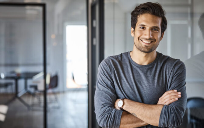 Portrait of smiling businessman standing with arms crossed at office