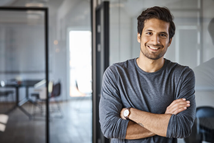 Portrait of smiling businessman standing with arms crossed at office